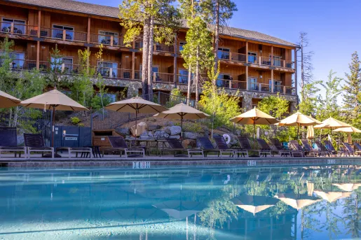 Outdoor pool surrounded by tan umbrellas and a wooden cabin in the background