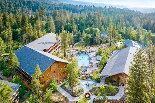 Exterior view of wooden hotel building with an outdoor pool, surrounded by tall trees