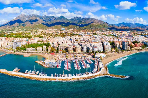 Sky view of a town in front of a beach, with large mountains in the background