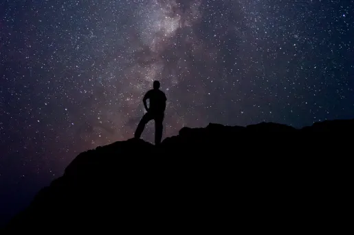 Silhouette of person standing on a cliff with the night sky in the background