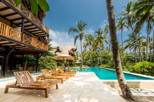 Outdoor pool surrounded by reclining, wooden chairs, with palm trees to the right