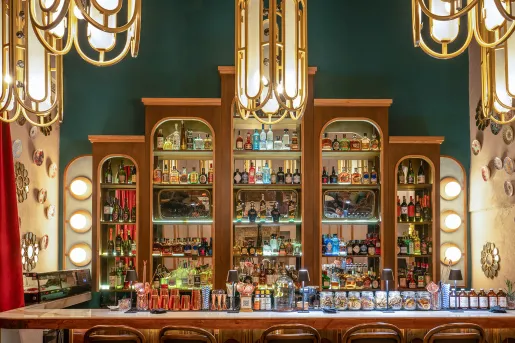 Bar with alcohol bottles on the wall and a counter full of glasses and small light fixtures