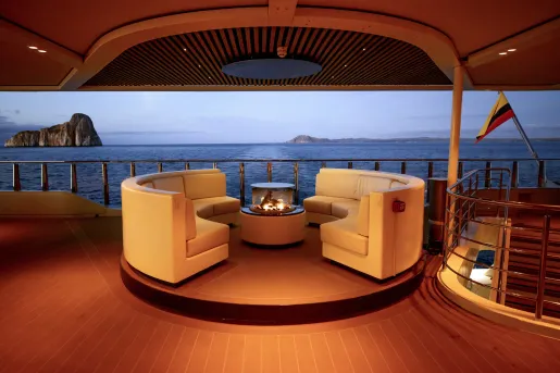 Cruise ship interior with circular sofas surrounding a fire pit, looking out to the ocean