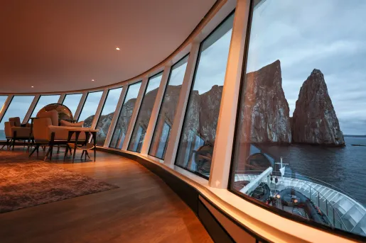 Cruise ship interior with sofas and wooden tables next to a large wall of windows