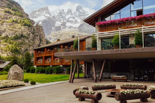 Exterior view of lodge hotel building with wooden benches in front and mountains in the background