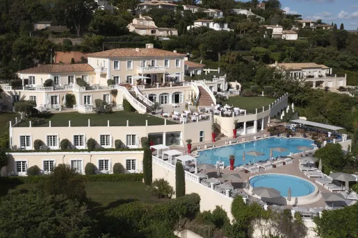Sky, exterior view of white hotel building with an outdoor pool, surrounded by trees