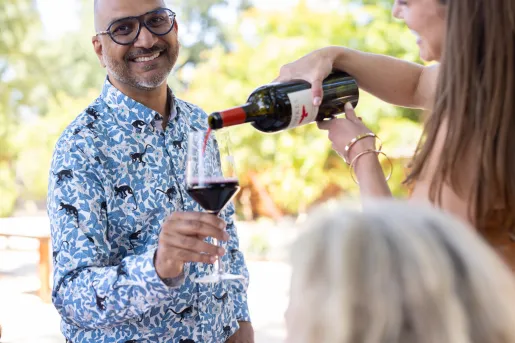 Man smiling, holding up a glass while a woman pours wine into the glass