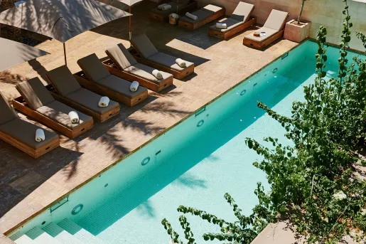 Outdoor pool surrounded by reclining green chairs and gray umbrellas