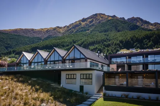 Exterior view of  a row of buildings with glass walls, and tall mountains in the background