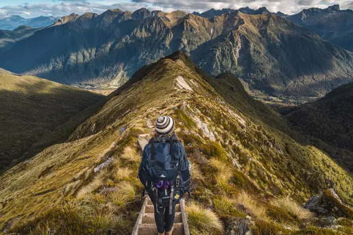 Woman descending a mountain with large mountains in the background