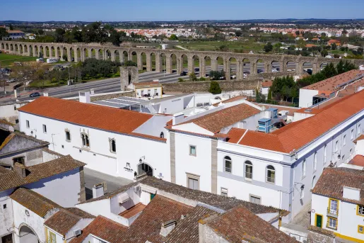 Exterior view of a large white building with red roofing, with a large stone bridge in the distance