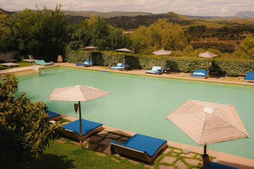 Outdoor pool with straw umbrellas and blue reclining beds surrounding the pool