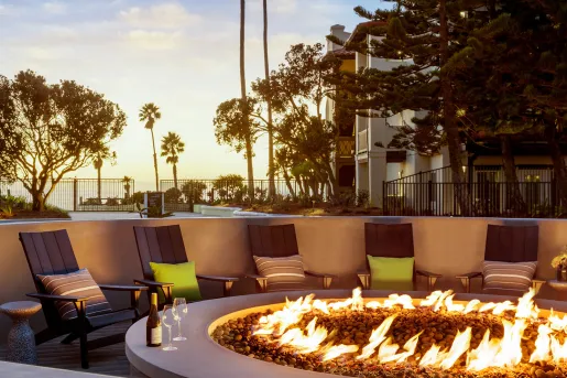 Outdoor firepit with chairs surrounding the pit, with trees and a sunset in the background