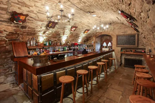 Bar and lounge in a cavern, with stone walls and alcohol lined up along the wall