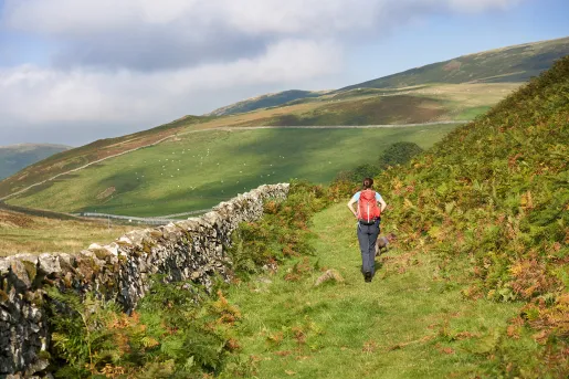 Woman walking on a grass trail looking towards large hills