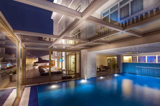 Pool illuminated with lights, in a room with large windows looking out to a hotel balcony