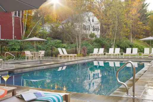 Outdoor pool, surrounded by white chairs and trees in the background
