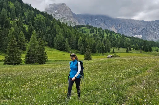 Woman walking through a grassy valley with a forest in the background