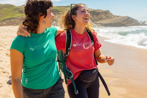Two women smiling with their arms around each other, walking on the beach