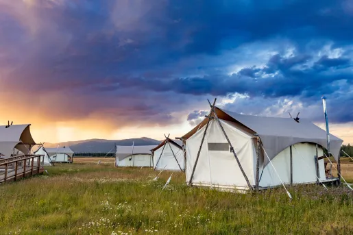 Bundle of luxury tents in a grassy valley with the sunrise in the distance