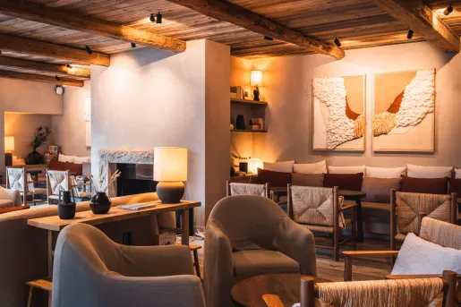 Warm and inviting hotel lounge featuring exposed wood-beam ceilings, upholstered armchairs, woven chairs, and soft ambient lighting. A stone fireplace, textured wall art, and natural materials create a cozy alpine atmosphere at the La Roche hotel in Montenegro..