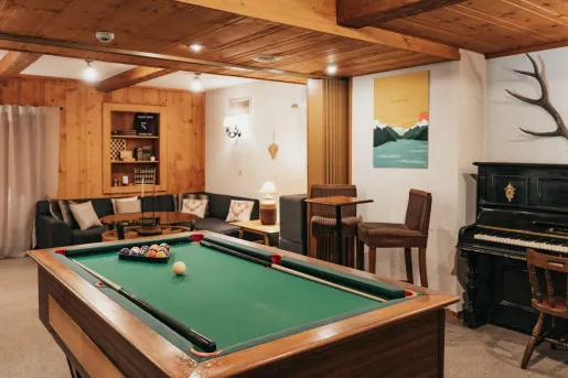 A rustic recreation room at Hôtel du Glacier, featuring a pool table, comfortable seating and a wooden piano against the wall.
