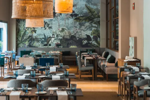 Restaurant with gray tables and dining chairs, with a large painting on the wall