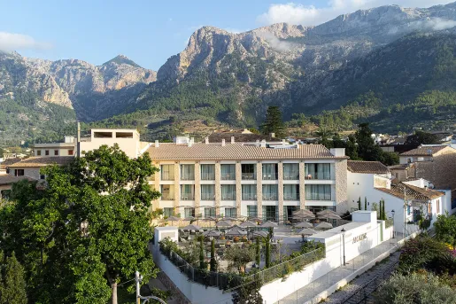 Exterior view of multi-floor hotel building, surrounded by tall trees and mountains in the background