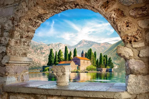 Stone arch with a view to a beige building surrounded by a lake