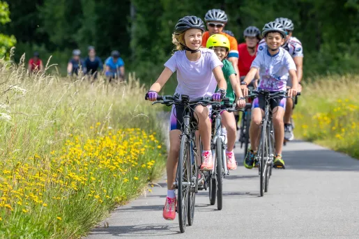 Group of kids and adults biking on a road surrounded by a tall grass field