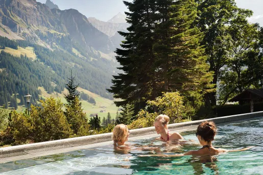 Three people standing in a pool looking out to large mountains