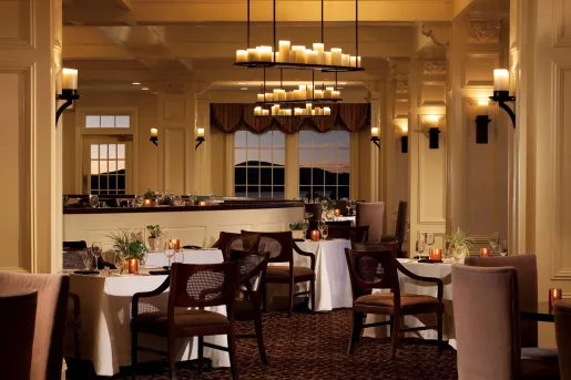 Restaurant dining area with white tablecloths on square tables, and beige chairs