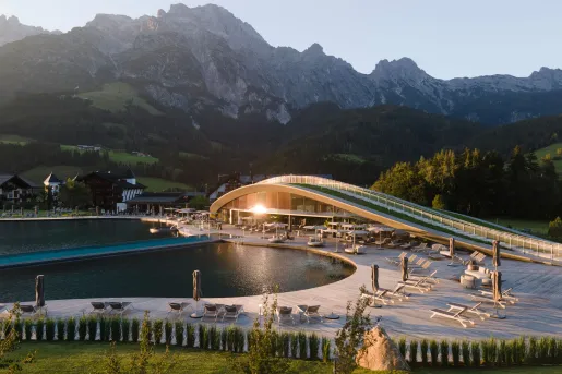 Large building with a large pool in front, and tall mountains in the background
