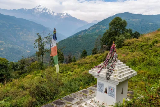 Top of a grassy hill with a stone statue and a colorful flag beside it