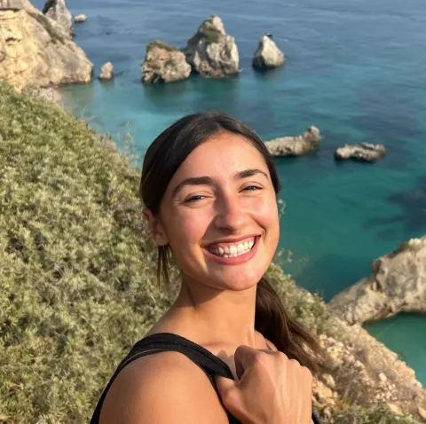 Woman smiling with a large cliff and ocean water in the background