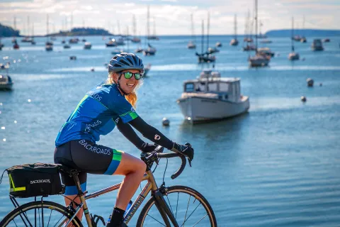 Guest biking with ocean and ships in background.