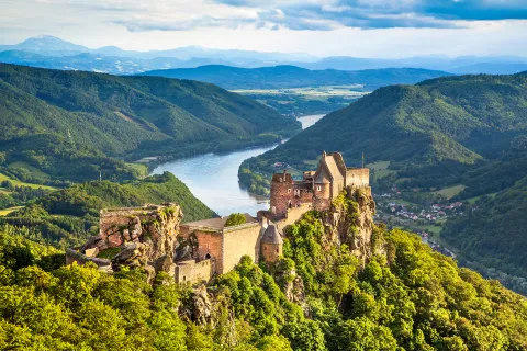 Forested landscape with Aggstein castle ruin and the Danube river at sunset in Wachau, Austria.