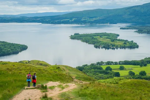 Two people descending a grassy hill towards a large lake