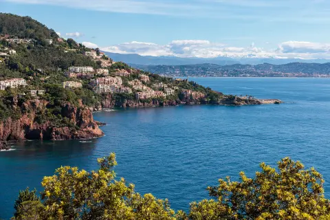 View of a bay in the French Riviera. A scenic town flows down from the hillside as blue water flows into the bay.