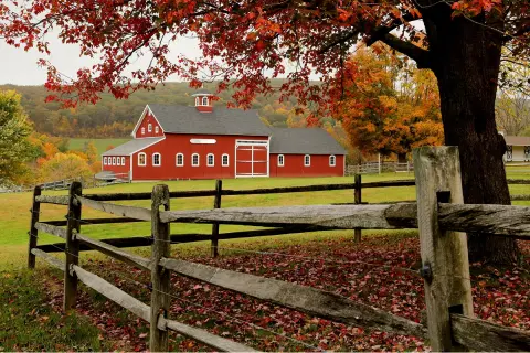 Red barn with a large field and wooden fence in front