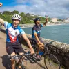 Two guests, cycling with fists raised, ocean to left.