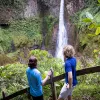 Two guests on forest path, looking down at forest, waterfall.