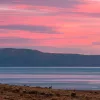 Wide shot of sunset vista, mountain, river, meadow, small horse all visible.