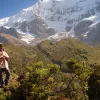 Local on hillside playing instrument, snowy mountains, hills behind them.