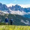 Two people with walking poles descending a grassy hill