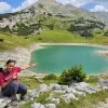 Woman sitting down and smiling, pointing at a small lake