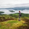 Woman standing on top of a grassy hill, looking out to smaller hills