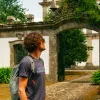 Man standing in front of a stone palace, surrounded by tall trees and bushes