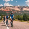 Group of 4 family members biking on an empty road, with a large valley and canyons in the background