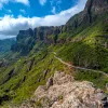 Curvy road in a mountain surrounded by large bushes with clouds in the sky